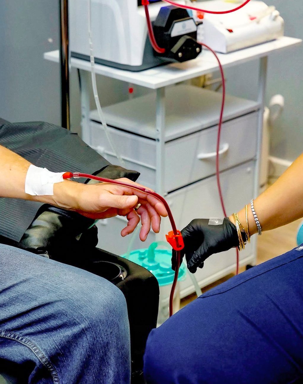 A gloved nurse managing the return line at a patient's hand